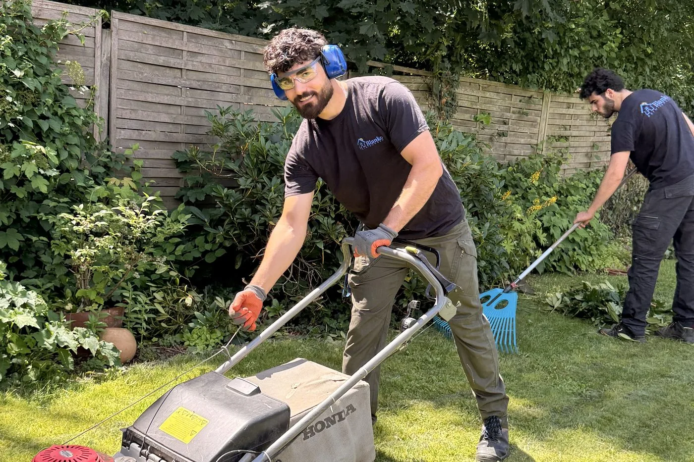 Zwei Mitarbeiter von Blanko Service beim Rasenmähen und Harken im Garten